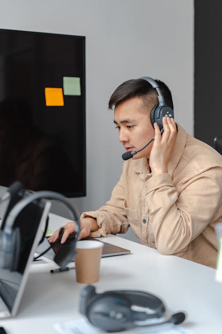 Focused call center agent using headset and laptop in modern office setting.